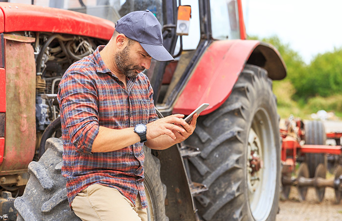 Farmer on phone next to tractor.